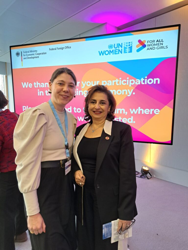 Annegret Krüger (left), President of the Women's Network for Peace (Frauennetzwerk für Frieden e.V. - IAW Associate) and individual member of IAW, and Sima Bahous (right), Executive Director of UN Women, pose for a photograph at the inauguration reception. They are standing in front of a large screen displaying the logos of the German Federal Foreign Office, BMZ and UN Women, alongside the slogan 'FOR ALL WOMEN AND GIRLS'.
