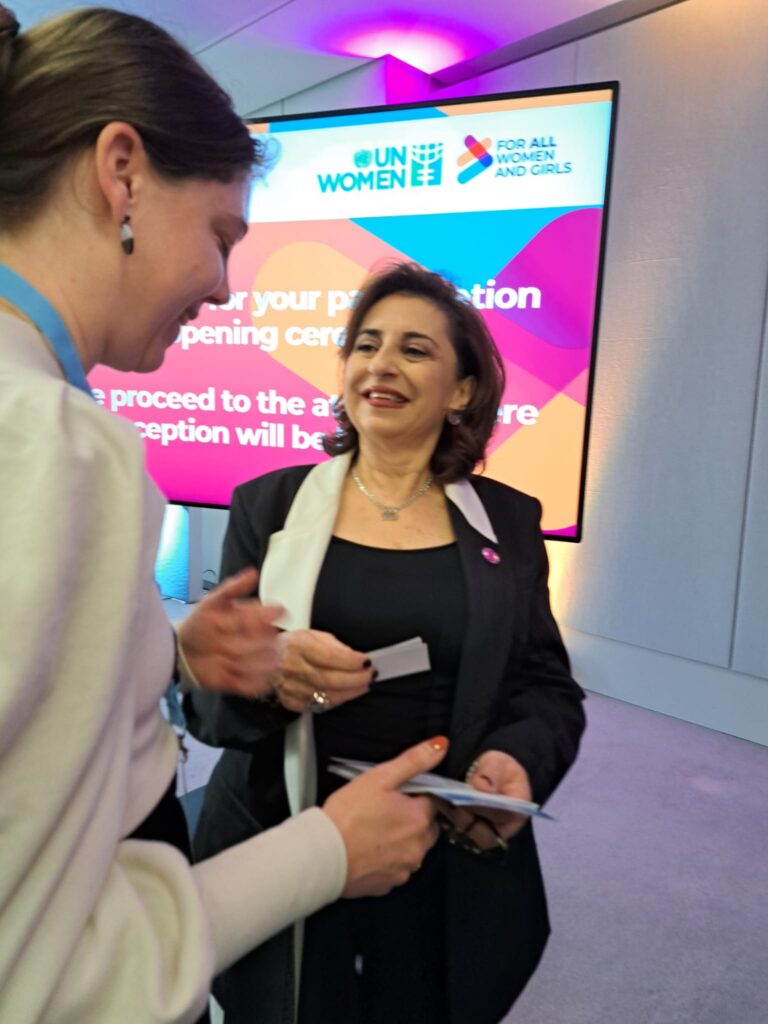 Annegret Krueger (left), President of Women's Network for Peace (Frauennnetzwerk für Frieden e.V.), and Sima Bahous (right), UN Women Executive Director, talking in front of a large screen displaying logos for the German Federal Foreign Office, BMZ, and UN Women, along with the slogan "FOR ALL WOMEN AND GIRLS".