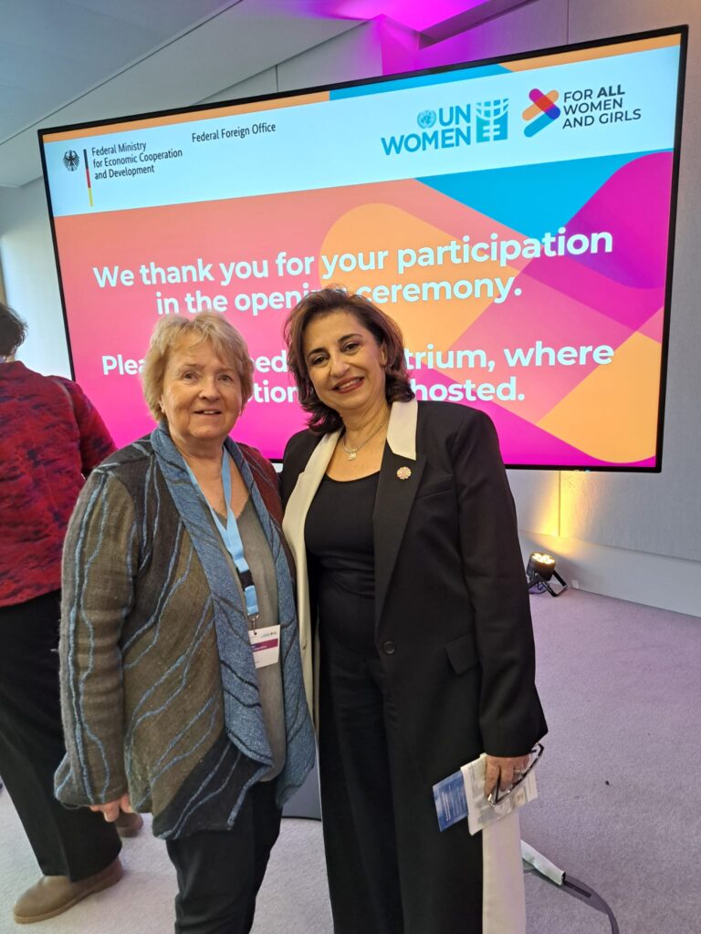 Heide Schütz (left), Honorary President of the Women's Network for Peace (Frauennetzwerk für Frieden e.V. - IAW Associate) and individual member of IAW, and Sima Bahous (right), Executive Director of UN Women, pose for a photograph at the inauguration reception. They are standing in front of a large screen displaying the logos of the German Federal Foreign Office, BMZ and UN Women, alongside the slogan 'FOR ALL WOMEN AND GIRLS'.